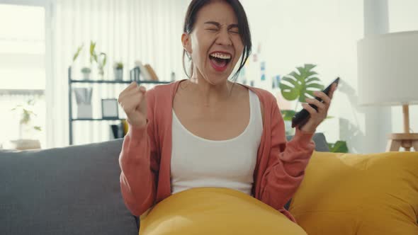 Beautiful asia lady sitting on sofa feel exciting with great news at home alt