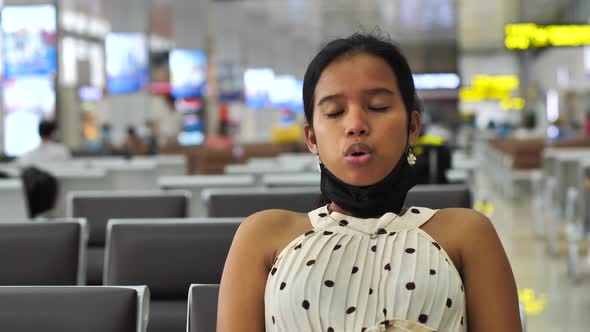 Asian Woman Sitting in the Waiting Area of Airport Taking Off Mask and Breathing alt