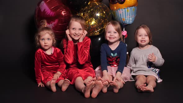 Little Kids Sitting on Floor with Colorful Balloons Behind.