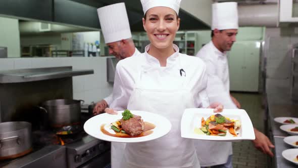 Smiling chef showing two dishes to camera alt