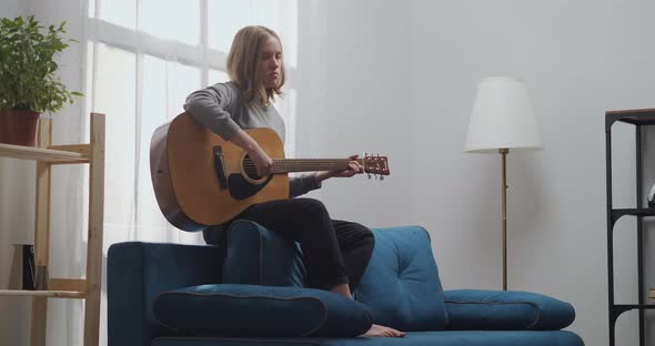 A Young Girl with Blonde Hair Is Enjoying Her Melody on an Acoustic Guitar with Beautiful Sunlight alt
