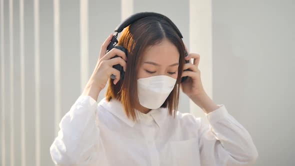 Woman covers a mask while wearing headphones under a building.