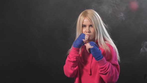 Blonde Female Athlete Is Exercising in Defense on Dark Smoky Background, Slow Motion alt