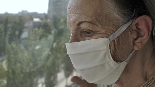 Older Woman in Face Mask Looks Through at the Window alt