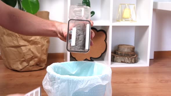 A Man Shakes Out Garbage Container From a Robot Vacuum Cleaner of Wool Dust Hair