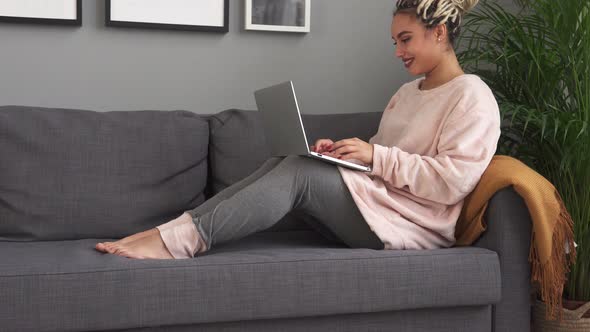 Happy Girl Using Laptop While Sitting on Modern Couch at Home