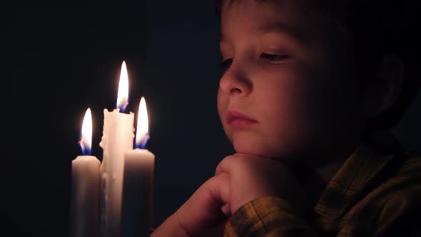 Little Cute Boy Prays in Front of a Burning Candle