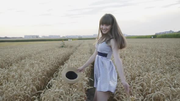 Happy Girl with Hat Running in Wheat Field, Turning and Smiling at Camera alt