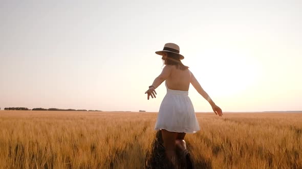 Happy Free Young Woman Runs in Slow Motion Across Field Touching Ears of Wheat with Her Hand