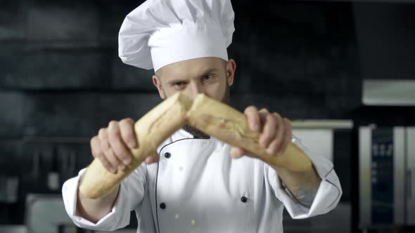 Male Chef Breaking French Bread in Slow Motion. Closeup Hands Breaking Bread alt