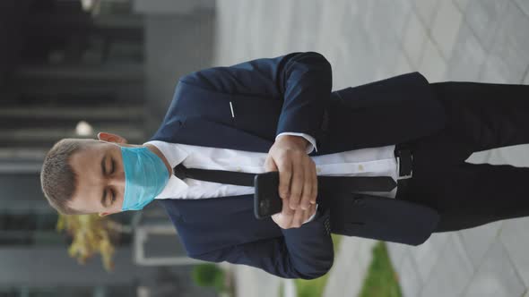 Man Wearing Protective Face Mask in the Street Looking at Smartphone Surfing Social Media App alt