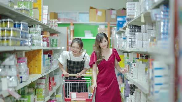 Two young Asian friends are strolling in a shopping cart while having fun in a supermarket.