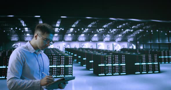 A Young Man Wearing Glasses Using Tablet While Working in Server Room in Contemporary Data Center