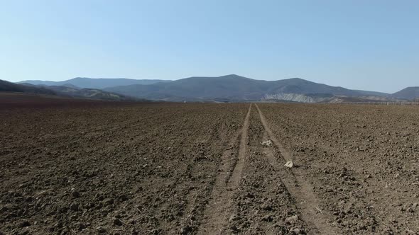 Flying Above Plowed Land Amid Mountains alt