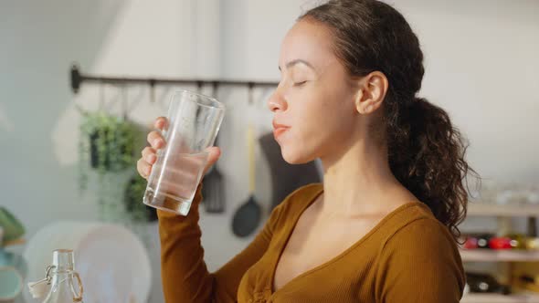 Young beautiful Latino woman drink or take a sips of mineral natural in cup for health care. alt