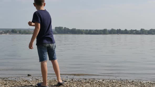 Teenage Boy in Shorts and Tshirt Throws Stones Into the River alt