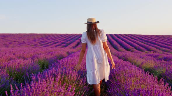 Young Woman in White Dress Walking Through a Lavender Field on Sunset