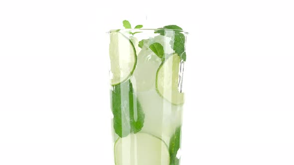 pour water in glass with with lime, mint and ice on white background. refreshing drink lemonade alt