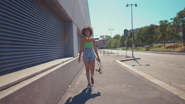 Beautiful young woman cruising around the city with her longboard. alt