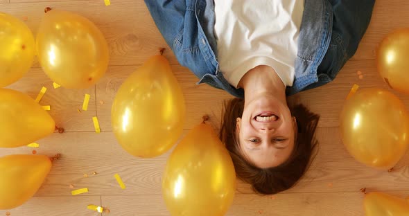 happy young woman at birthday party smiling and having fun of lying on the floor with gold confetti 