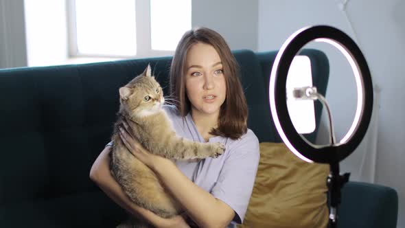 Woman Blogger with Her Cat Is Recording Video on Smartphone Using Ring Lamp