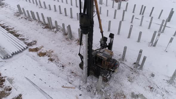 Aerial drone view of a pile bore machine and worker at winter construction site 04 alt