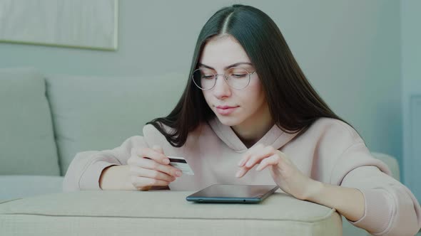 Young Caucasian woman with glasses tapping on tablet making online purchases