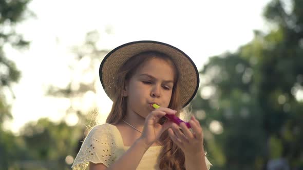 Pretty Cute Girl Blowing Party Whistle Sitting in Sunrays Outdoors alt
