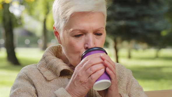 Happy Elegant Grandmother of Retirement Age Sitting on Park Bench Drinking Tea alt