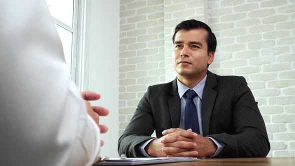 Handsome Hispanic businessman in formal suit talking with applicant at the table