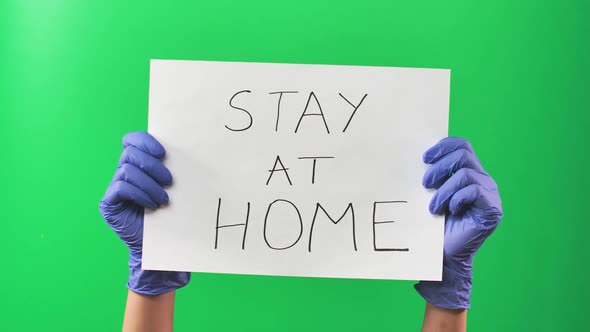 Hands Doctor Woman in Blue Gloves Holding a Sign with an Appeal To Stay at Home. Green Screen. Close alt