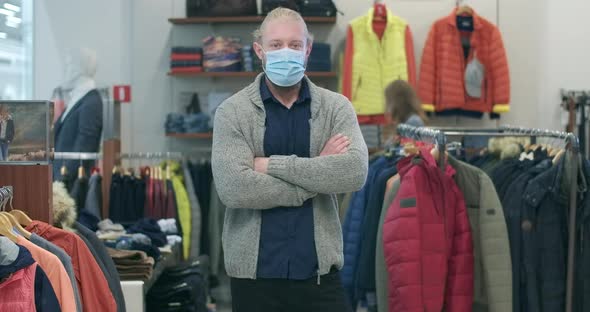 Young Caucasian Man in Covid-19 Face Mask Crossing Hands and Looking at Camera As Blurred Woman alt