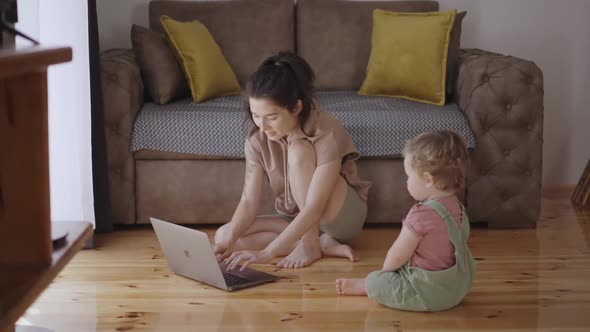 Mother Multitasking Holding Baby Infant and Using Computer Laptop at Home alt