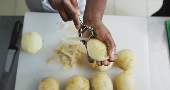 Midsection of african american female chef peeling potatoes in restaurant kitchen alt