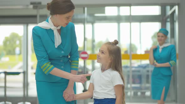 Charming Cheerful Woman in Stewardess Uniform Talking To Cute Little Caucasian Girl in Airport alt