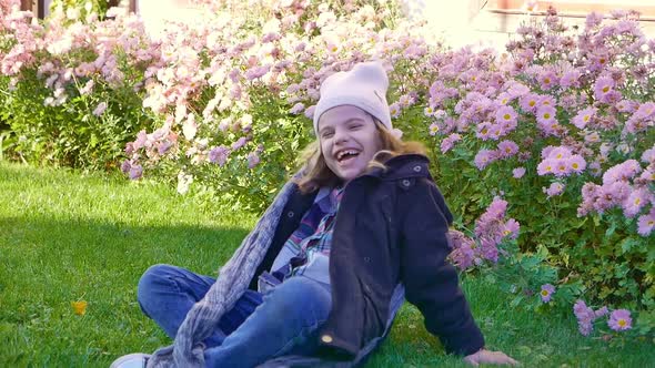 Happy Girl Laughs on a Lawn in a Flower Garden