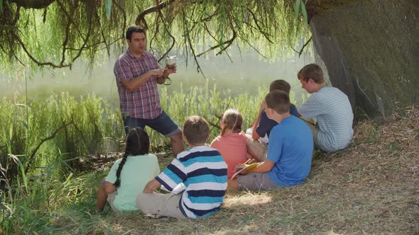 Kids at outdoor school have group lesson by pond