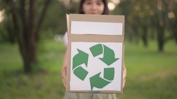 Closeup Cardboard Box with Green Recycling Sign Stretched to Camera and Blurred Teenage Ecoactivist alt