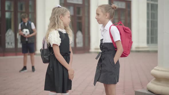 Schoolgirls Talking Before Lessons As Blurred Boy Standing with Football Ball at the Background alt