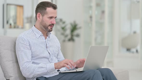 Young Man Celebrating Success on Laptop at Home  alt