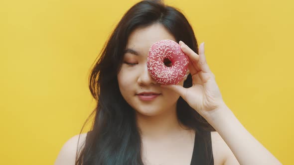 Attractive Asian Woman Having Fun Putting Donuts Over the Eyes alt