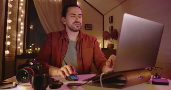 A Young Handsome Male Photographer and Videographer Works at Home on a Laptop alt