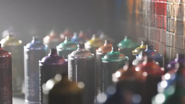 Used, colorful spray paint cans standing in front of a painted brick wall. 4KHD alt