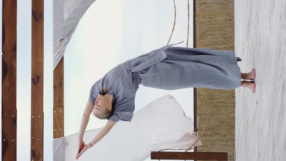 Young Blonde Woman in the Blue Robe Doing Yoga Pose at Terrace alt