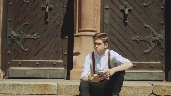 Portrait of a Handsome Young Man Wearing Casual Clothes and Using Smartphone on the Urban Street alt