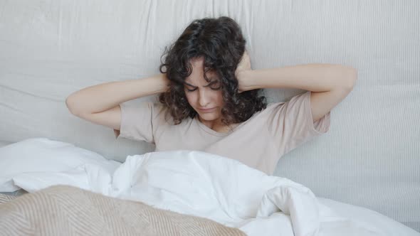 Unhappy Young Woman Can't Sleep Because of Loud Noise Covering Ears with Hands in Bed alt