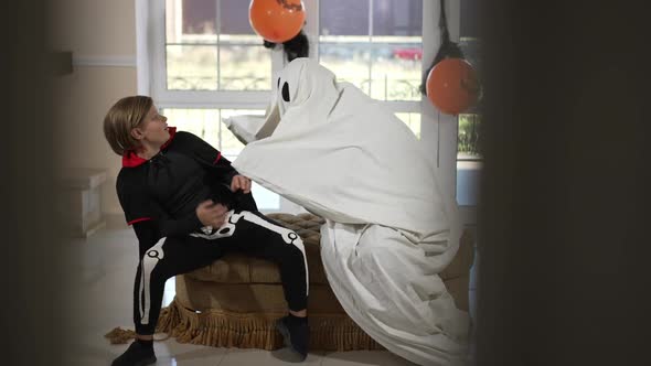 Wide Shot Scary Ghost Frightening Cute Boy Sitting in Living Room on Halloween alt