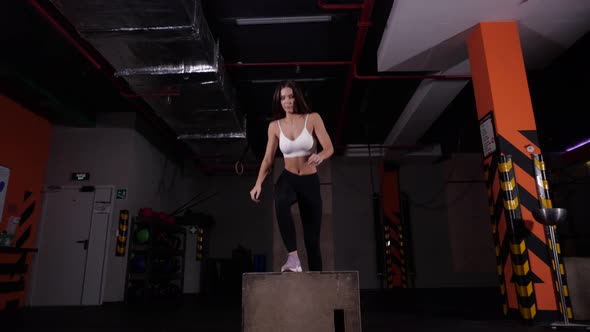 Beautiful Fitness Athlete Performs Box Jumping in the Gym in a White Sports Top