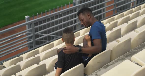 Diverse Father and Son Hugging and Watching Match on Stadium alt