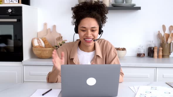 Positive African American Girl with Headset Freelancer Advisor Student Sits at Desk in the Kitchen alt